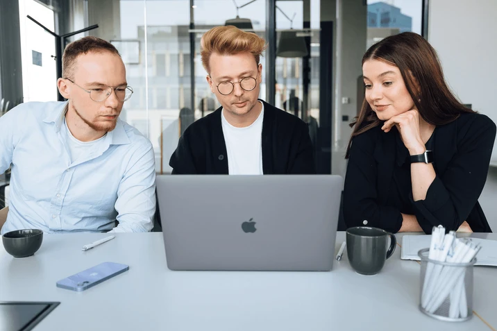 Trójka młodych pracowników współpracuje przy laptopie w nowoczesnym biurze podczas spotkania zespołowego