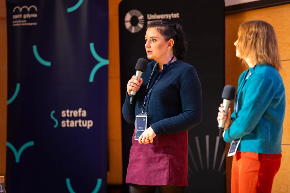Dwie kobiety na scenie podczas prezentacji na konferencji startupowej z mikrofonami w rękach