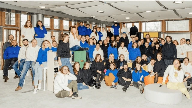 Duża grupa pracowników w biurze pozująca wspólnie do zdjęcia w różnych kolorach ubrań na jasnej przestrzeni