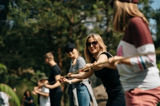 Grupa ludzi na świeżym powietrzu uczestniczy w zabawie zespołowej, tworząc atmosferę współpracy i integracji