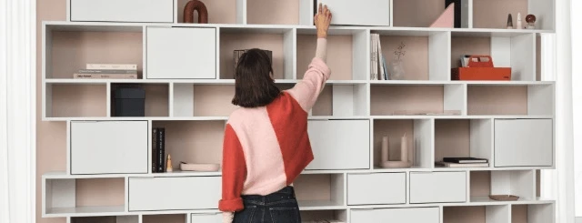 Osoba wybiera element z nowoczesnej białej półki w jasnym i stylowym wnętrzu biurowym