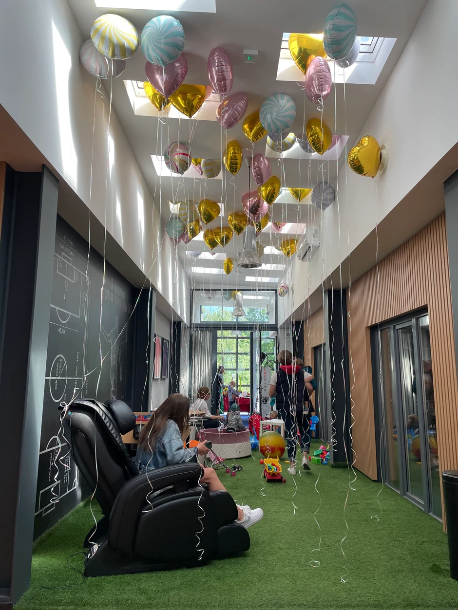 Przestronne biuro z zielonym dywanem, dekorowane balonami i strefą relaksu dla dzieci i pracowników